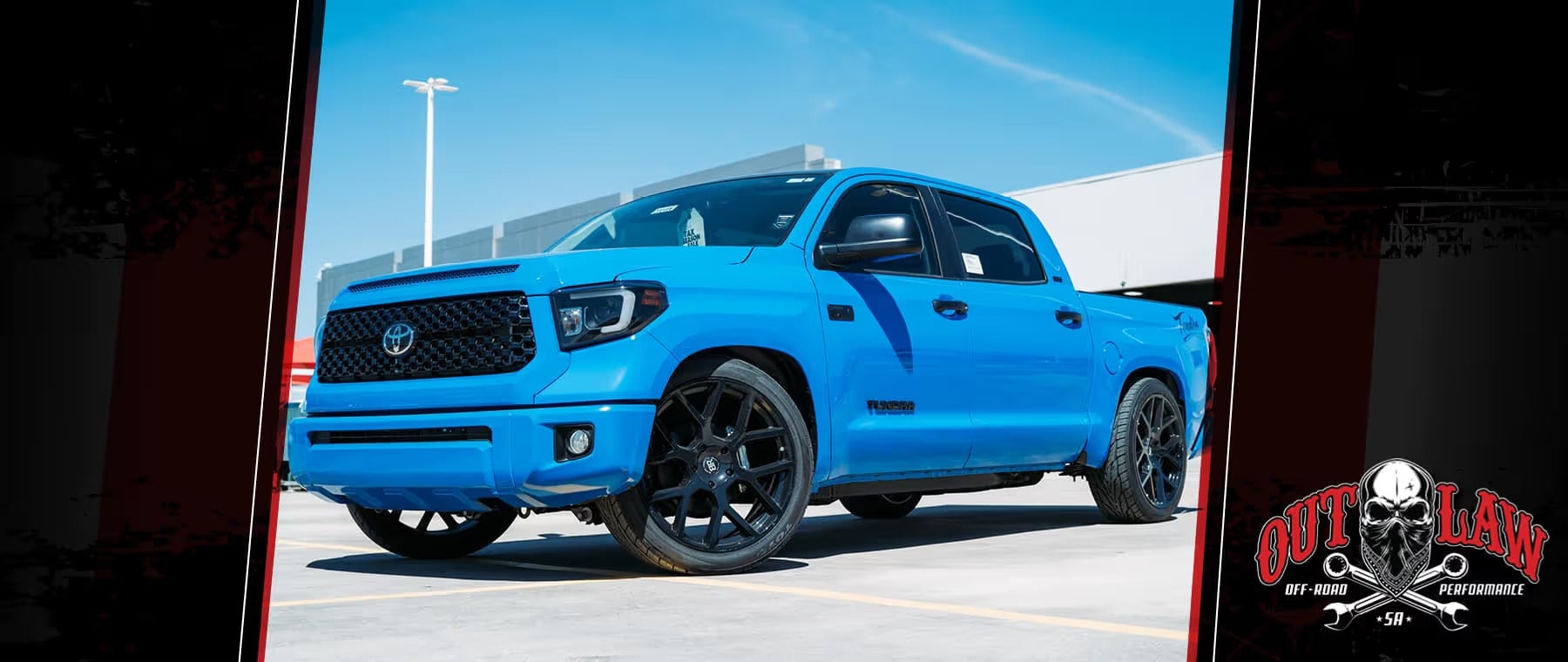Bright blue Toyota Tundra truck with black rims and a lowered stance, parked in front of a building under a clear sky.