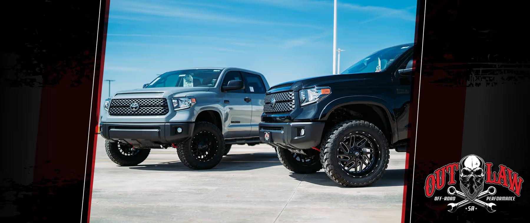 Two lifted Toyota Tundra trucks, one silver and one black, with large off-road tires, parked side by side on pavement under a blue sky.